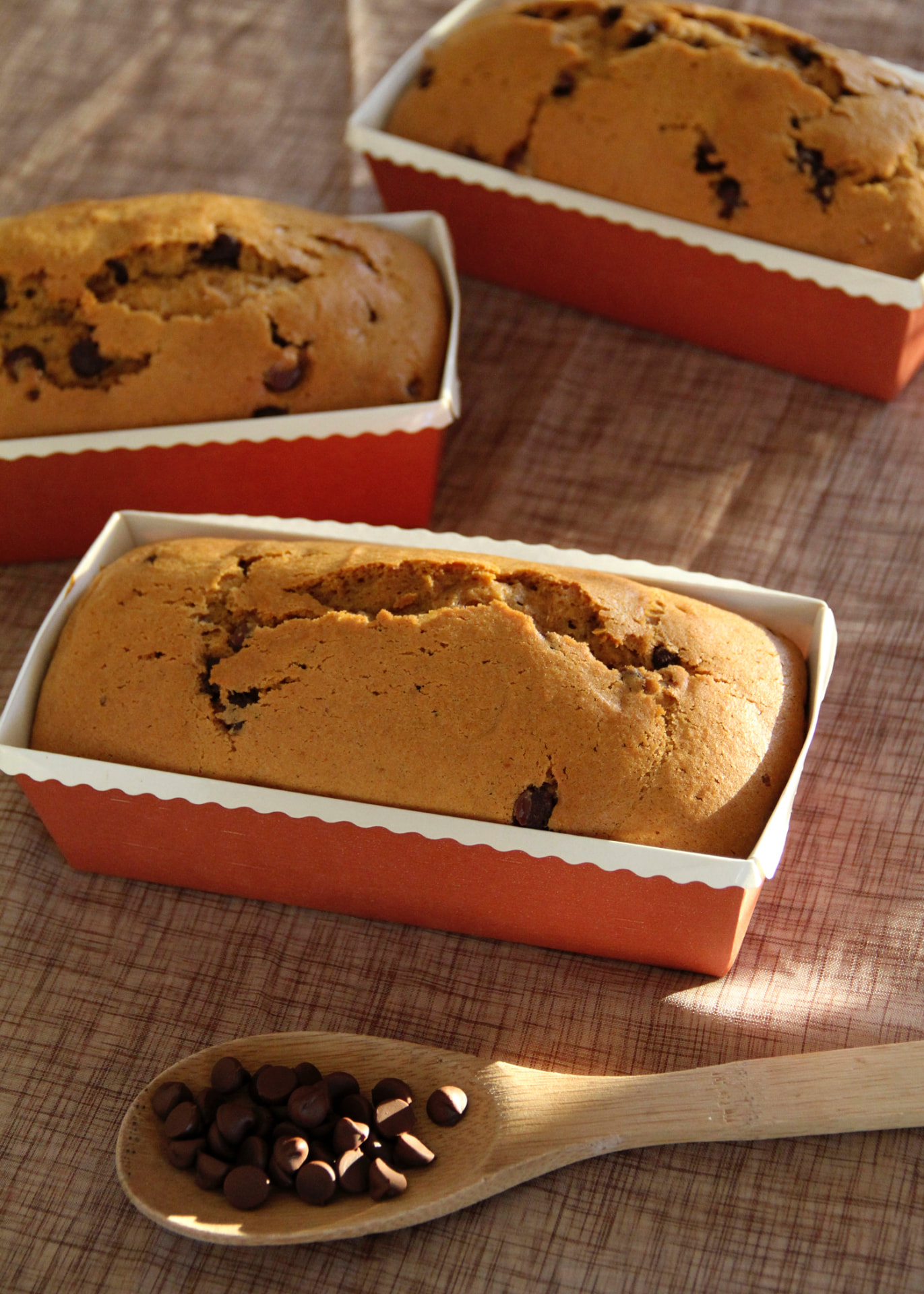 Pumpkin chocolate chip teacake loaves in orange baking pans beside a spoonful of chocolate chips